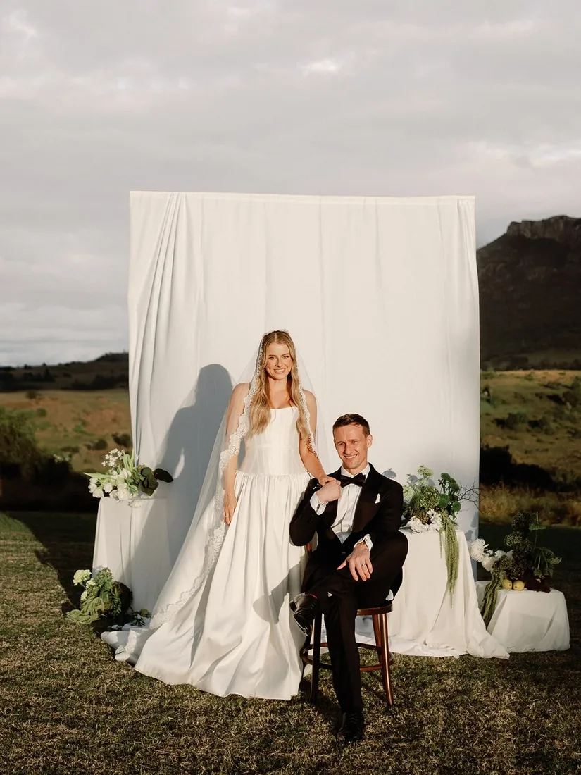 Samara and Ryan seated together in front of a white fabric backdrop with mountain views