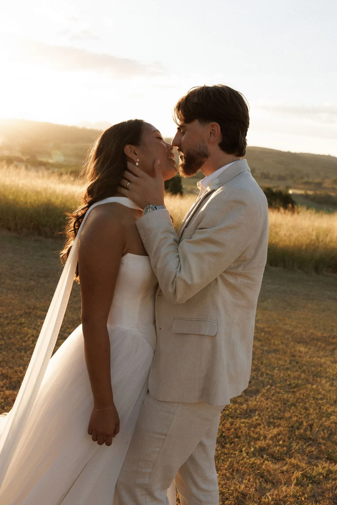 Hamish and Sarah kissing at golden hour in a paddock of long grass