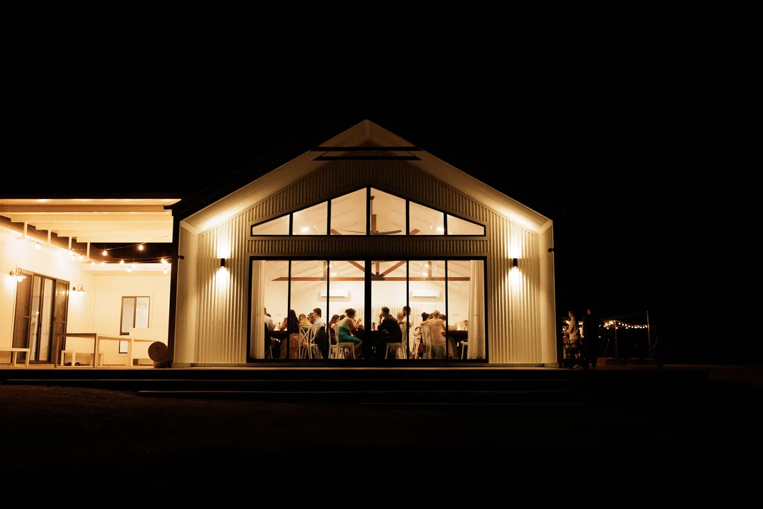 The reception barn lit up at night, guests seated inside