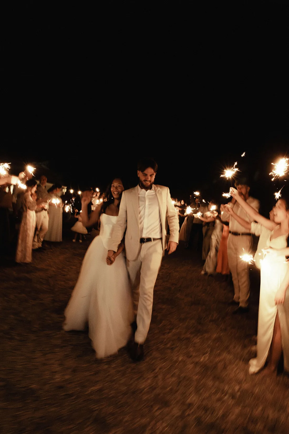 Hamish and Sarah walking through a sparkler send-off at night