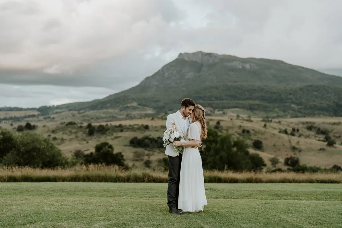 Sarah and Rhys embracing on the lawn at Maroon Hill Estate, with Mount Maroon behind them
