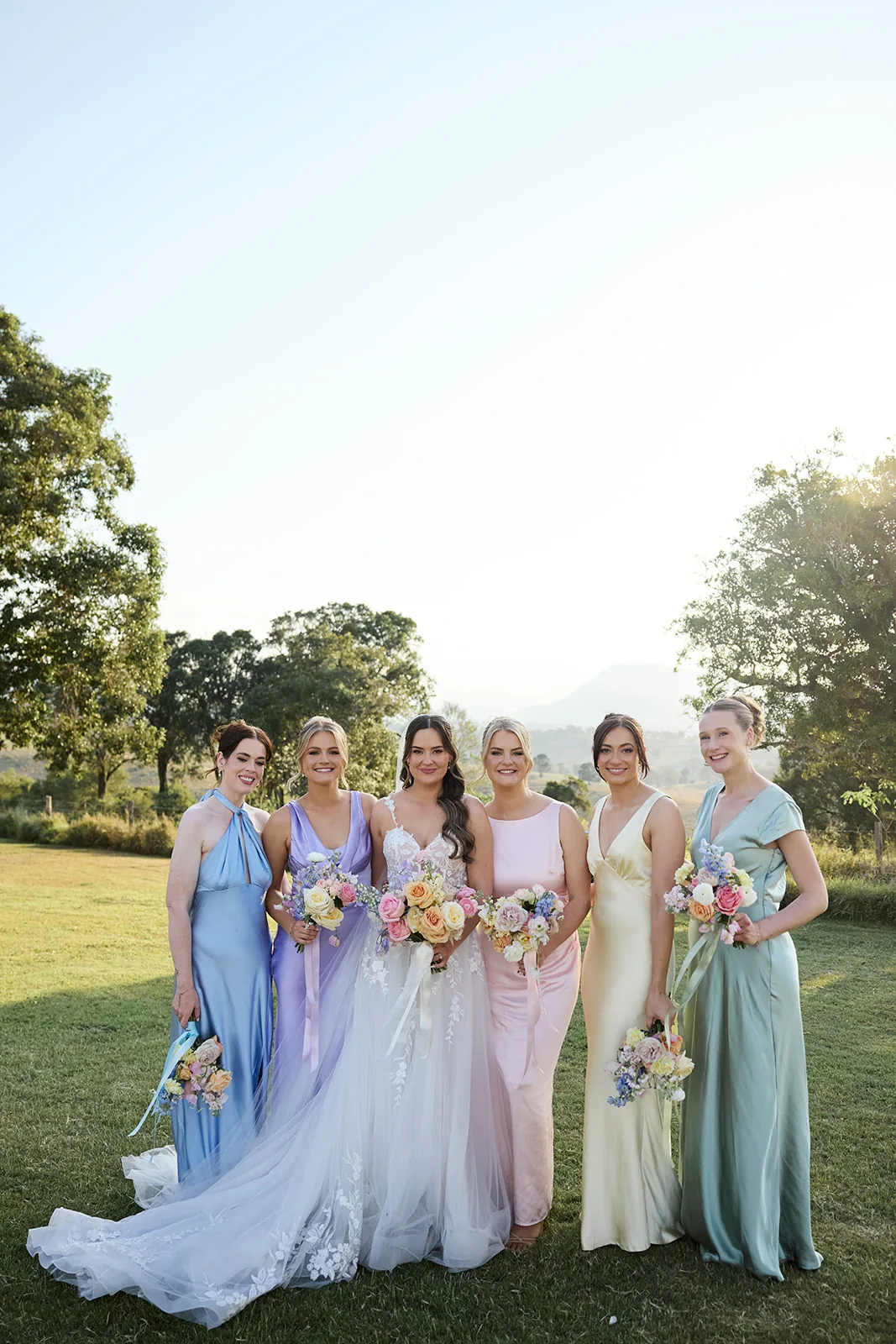 Full bridal party group photo in mismatched pastel gowns, mountains behind