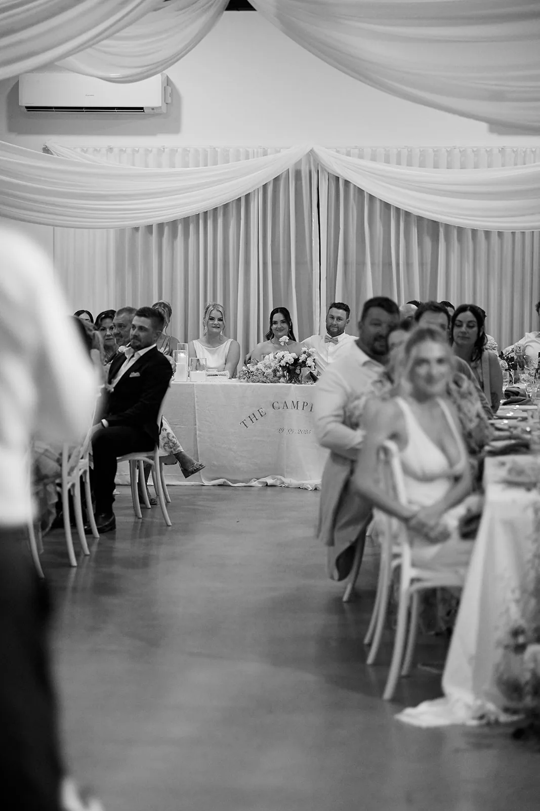 Black and white candid of guests laughing and reacting at the reception table