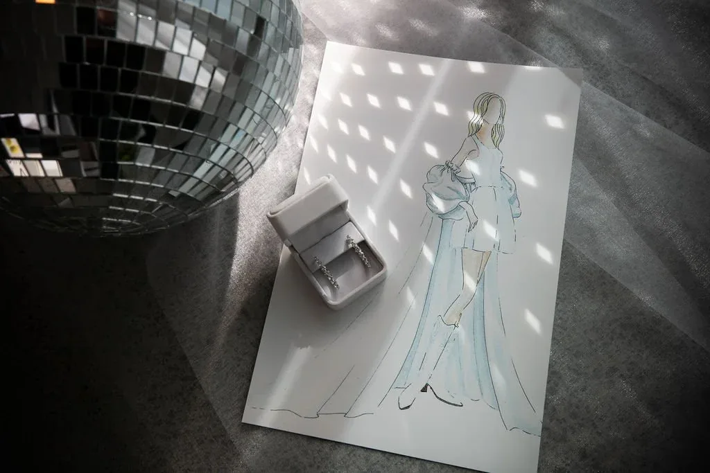 Fashion illustration of a bridal gown sketch styled beside a disco ball and ring box