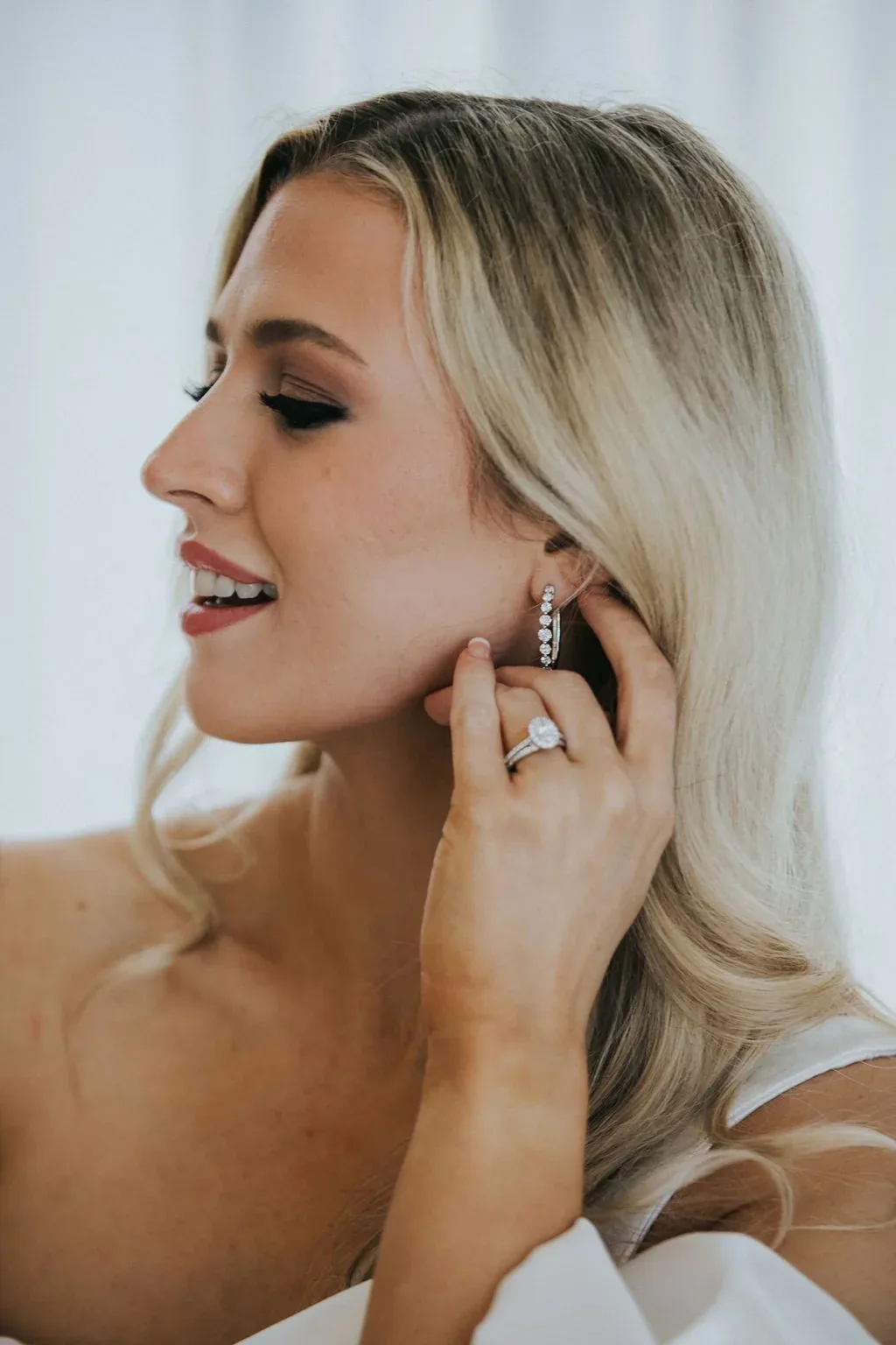 Close-up of the bride fastening a diamond drop earring, wearing a diamond ring