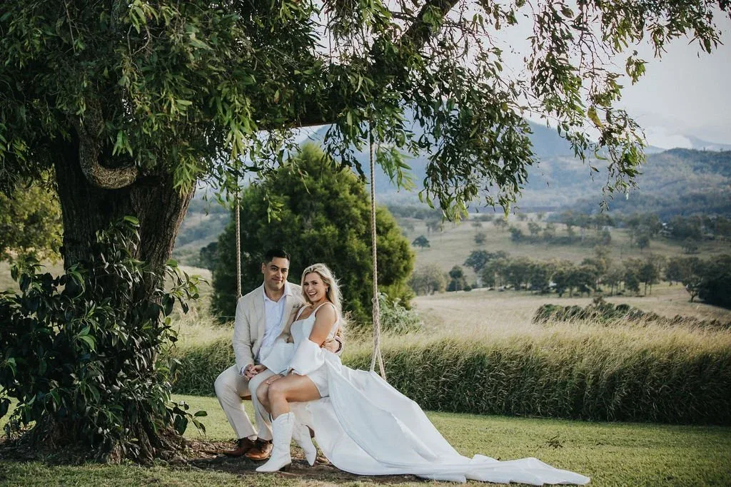 Bride and groom sitting together on a tree swing overlooking the hills