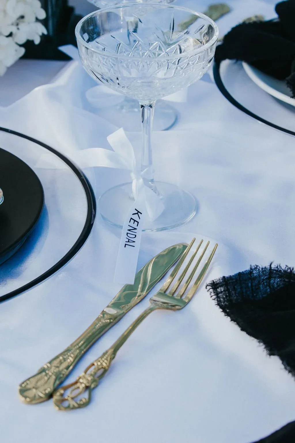 Place setting with gold cutlery, a crystal coupe glass and a name tag reading Kendal