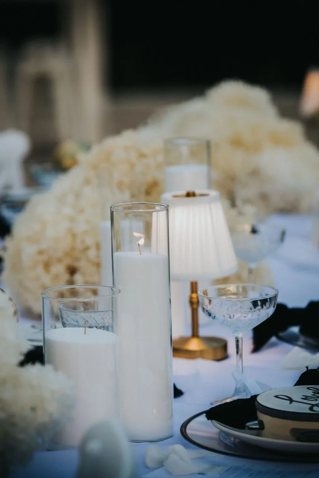 Table setting with pillar candles, a mini lamp and dried white florals in the evening light