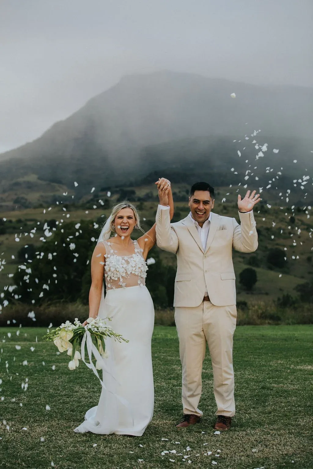 Bride and groom celebrating with confetti falling around them, misty mountain backdrop