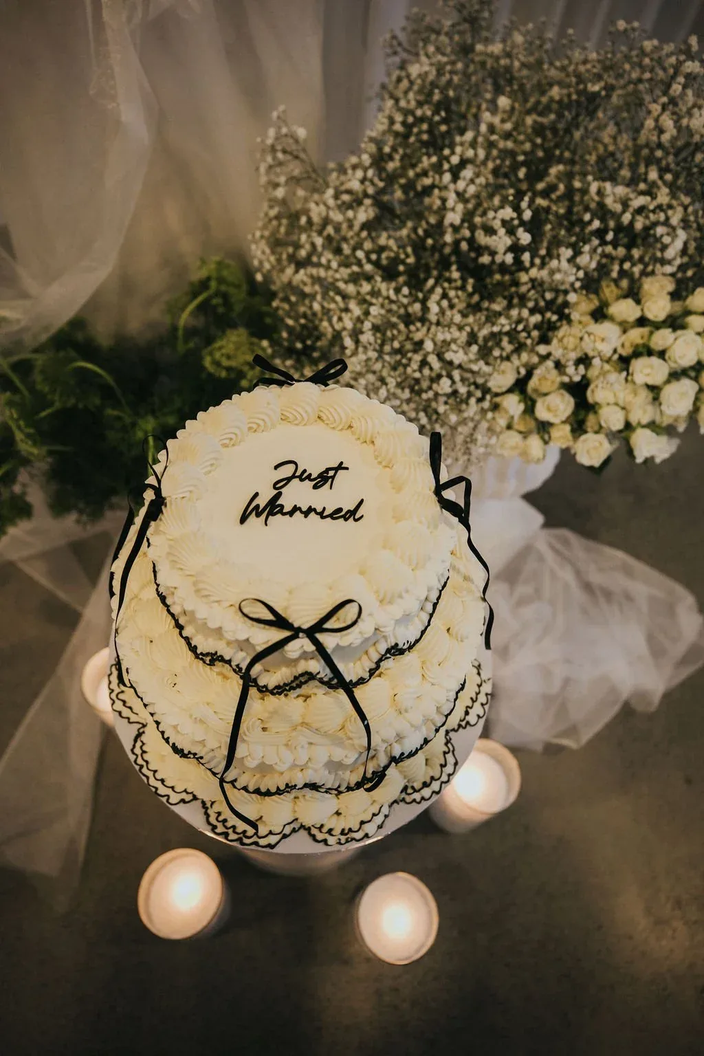 Overhead view of a Just Married cake with black ribbon detail, surrounded by candles and gypsophila