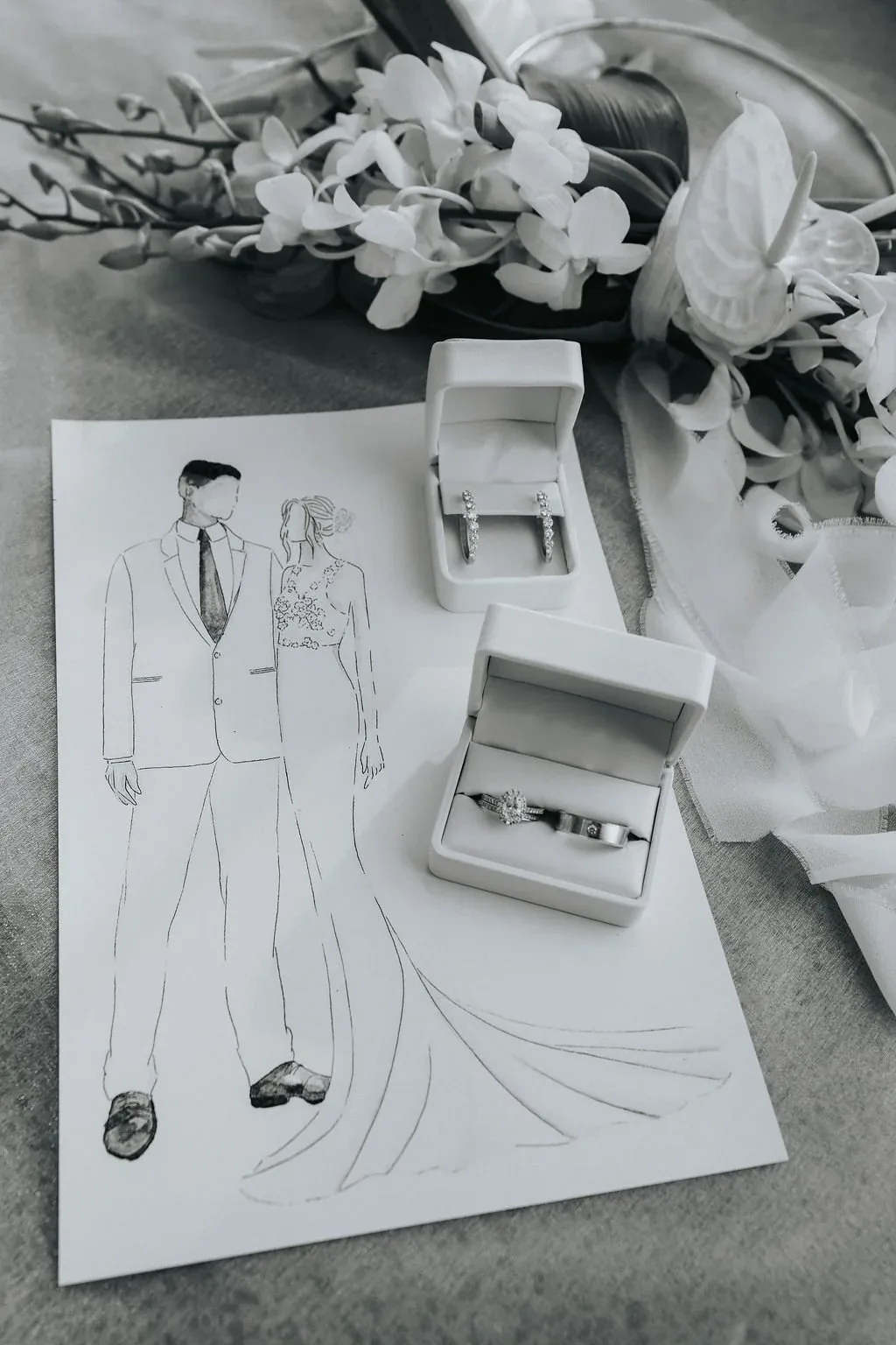 Fashion illustration of the bride and groom's outfits styled beside diamond earrings and a ring box