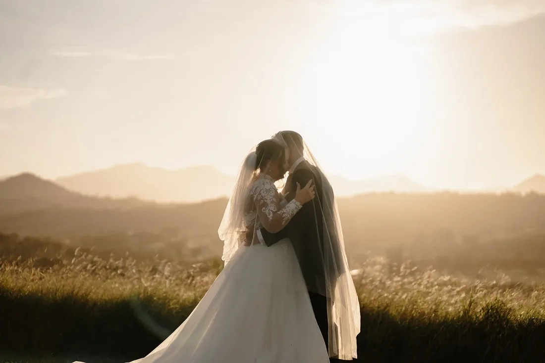 Tylah and Brock kissing under a veil at golden hour at Maroon Hill Estate