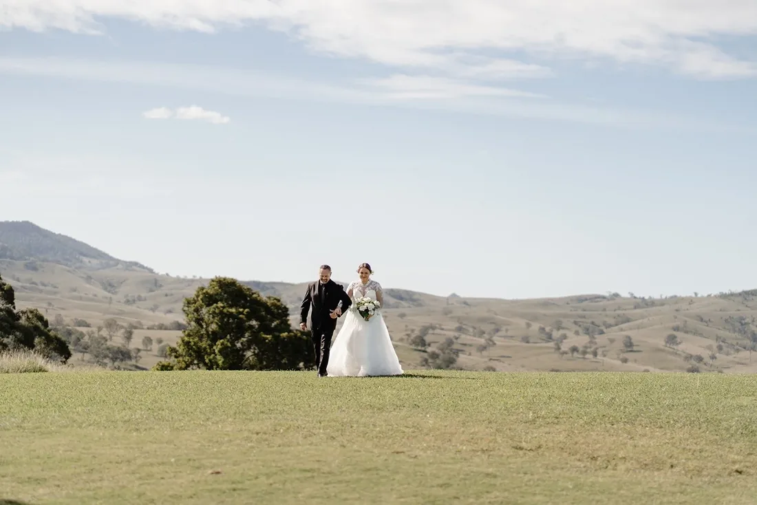 Tylah and Brock walking across the lawn hand in hand with rolling hills behind