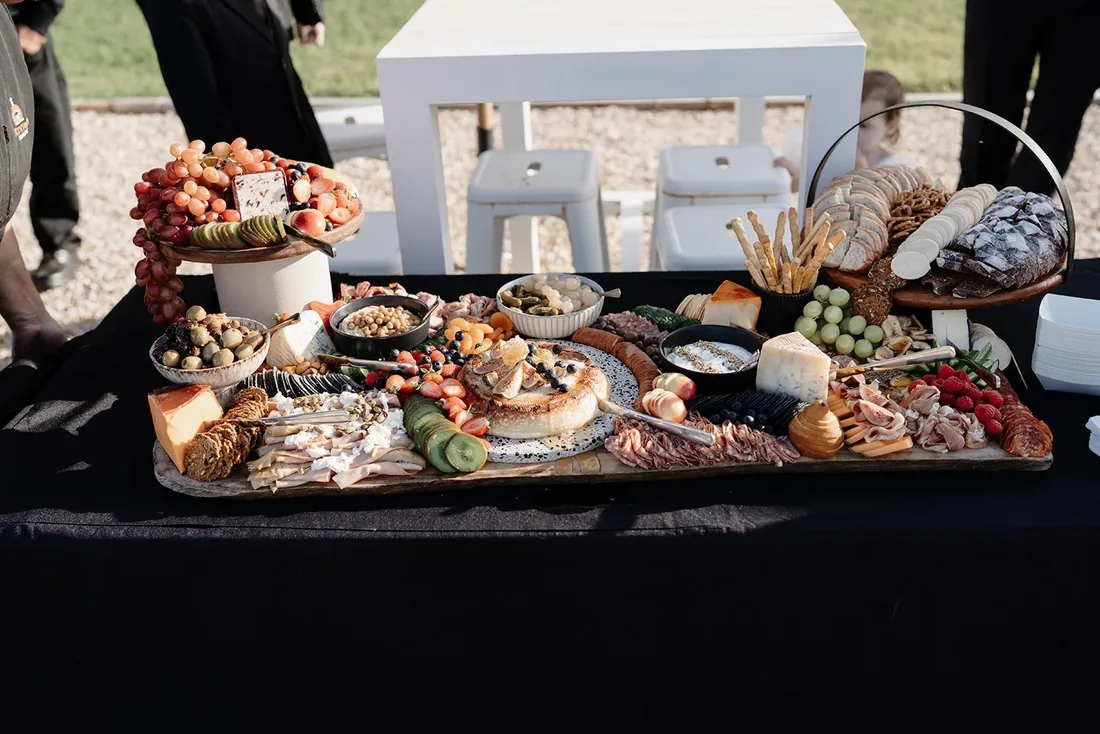 Grazing table spread with cheeses, charcuterie, fruit and crackers styled on a dark cloth