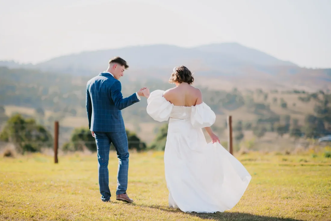 Groom in a check suit twirling his partner in a billowing white gown across the lawn