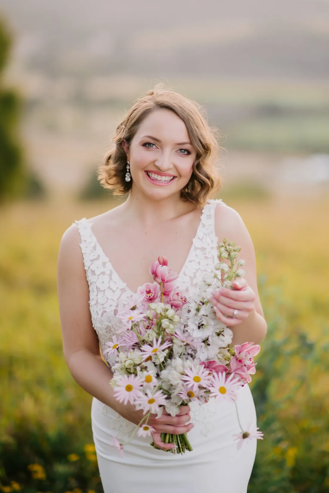 Bride smiling and holding a bouquet of pink and white daisies, mountains in the background