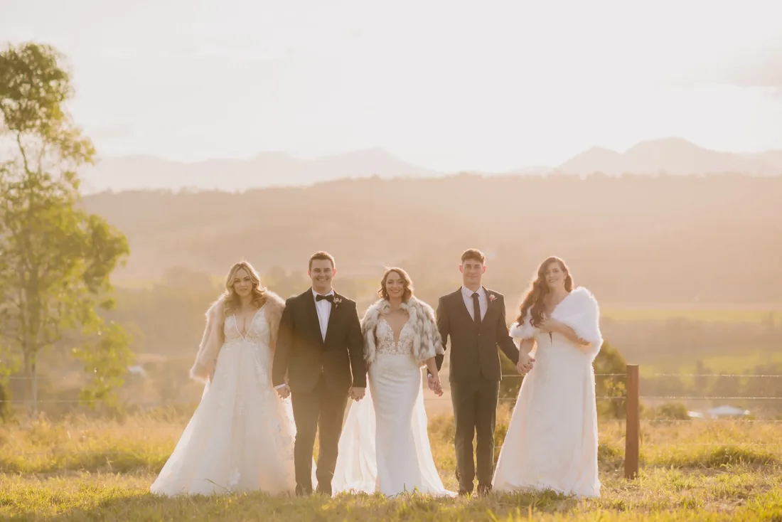 Five models in mixed bridal and eveningwear styles standing together at golden hour