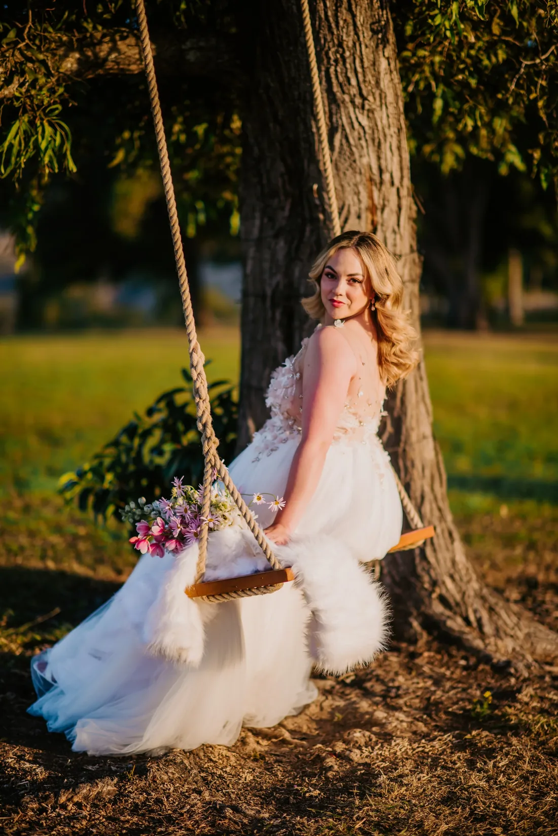 Bride sitting on a tree swing in a beaded bridal gown, holding a wildflower bouquet