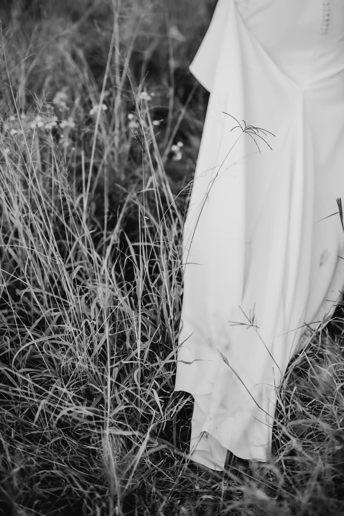 Black and white close-up of a bridal gown skirt against long grass