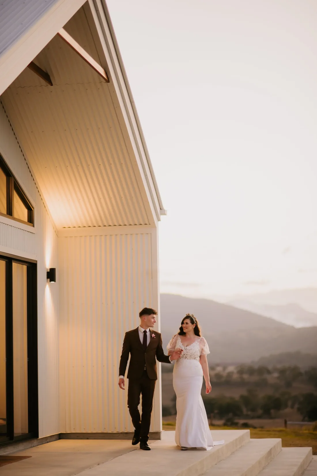 Couple walking together outside the reception building at dusk, mountain views behind