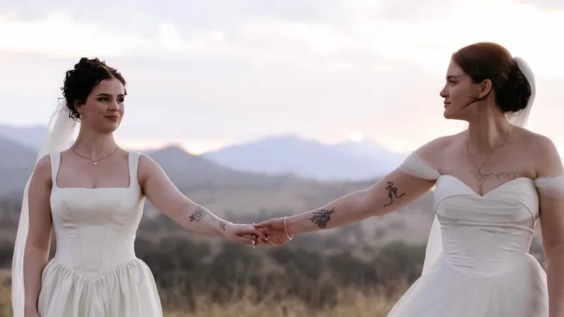 Kaitlyn and Imogen holding hands in their wedding dresses, the ranges behind them at dusk